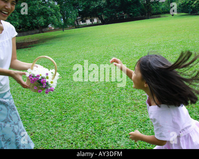 Giovane donna tenendo un cesto di fiori con sua figlia a correre verso di lei Foto Stock