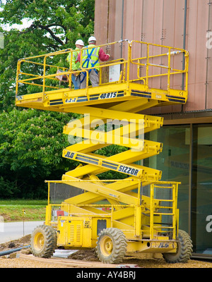 Elevatore a pantografo sul sito di costruzione che mostra i lavoratori con equipaggiamento di sicurezza Foto Stock