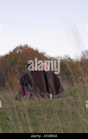Coppia giovane seduto nel campo vista posteriore donna sorride guardando la fotocamera Foto Stock