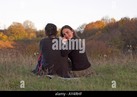 Coppia giovane seduto nel campo vista posteriore donna sorride guardando la fotocamera Foto Stock