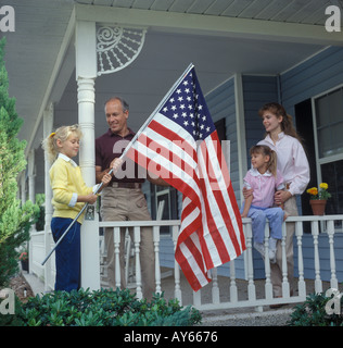 Famiglia di quattro mettendo a bandiera americana sul portico anteriore Foto Stock
