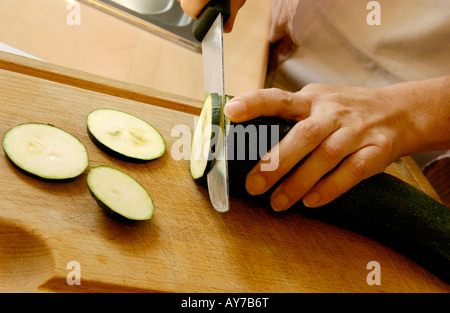 Donna tritare le zucchine ortaggi in cucina su un tagliere Foto Stock