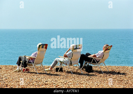 Tre persone in sedie a sdraio sulla spiaggia Seatown nel Dorset Regno Unito Regno Unito Foto Stock