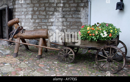 Legno decorativo cavallo tirando un vecchio carro di legno riempito di fiori, impostare nella parte anteriore del vecchio edificio di mattoni bianchi cortile di pietra Foto Stock