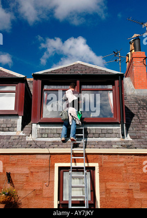 Un detergente per vetri su una scala pulisce la parte superiore delle finestre di un 2 storied house Foto Stock