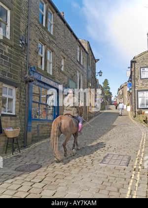 Una donna su un marrone a cavallo fino la strada principale lastricata in pietra nel villaggio turistico di Howarth West Yorkshire Foto Stock