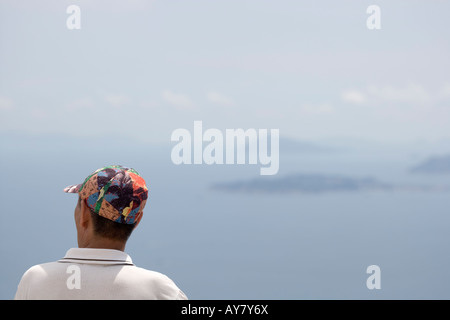 Uomo cinese indossando un vivacemente colorato cappello da baseball che guarda verso il mare della Cina del Sud da Victoria Peak Hong Kong Cina Foto Stock