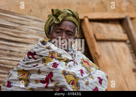 Un'anziana donna in Togo, Africa occidentale è avvolto in uno scialle e di seduta al di fuori della propria casa Foto Stock