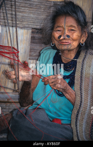 Apatani donna tribale con tradizionalmente faccia tatuata e tessitura noseplugs al di fuori del suo longhouse in Arunachal Pradesh, India Foto Stock