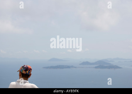 Uomo cinese indossando un vivacemente colorato cappello da baseball che guarda verso il mare della Cina del Sud da Victoria Peak Hong Kong Cina Foto Stock