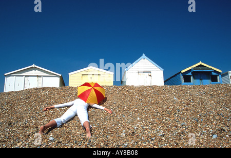 Donna sdraiata sulla spiaggia di ciottoli di fronte spiaggia capanne Hastings East Sussex England South Coast REGNO UNITO Inghilterra Gran Bretagna Foto Stock