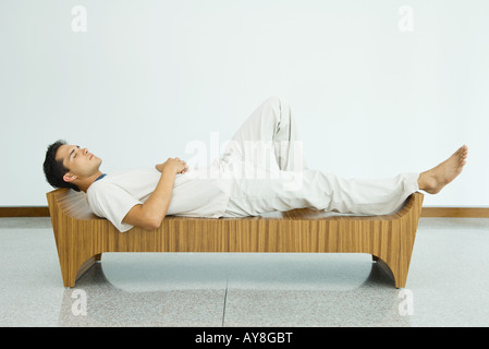 Uomo disteso sul banco di lavoro con gli occhi chiusi, vista laterale Foto Stock