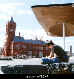 Studente giovane seduto fuori dall'Assemblea Nazionale del Galles e vista dell'edificio Pier Head a Cardiff Bay South Glamorgan Wales UK KATHY DEWITT Foto Stock