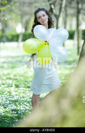 Giovane donna camminare in prato, tenendo palloncini, guardando lontano Foto Stock