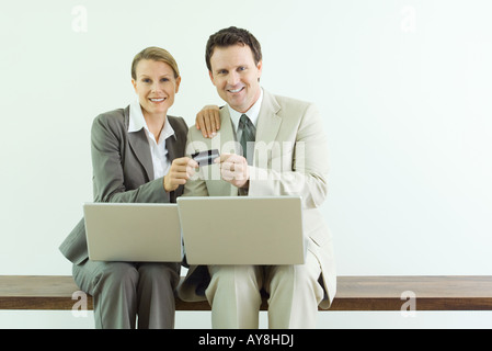 L uomo e la donna seduta, tenendo carta di credito insieme, sia vestito in abiti con il computer portatile Foto Stock