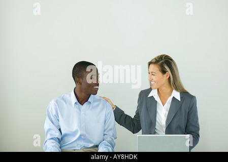 Imprenditrice seduta accanto al ragazzo adolescente con la sua mano sulla spalla, entrambi sorridendo a ciascun altro Foto Stock