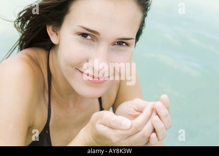 Giovane donna il contenimento dell'acqua nelle mani a tazza, sorridente in telecamera, close-up Foto Stock