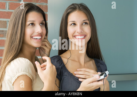 Teenage gemelle ascoltando mp3 player insieme, sia sorridente e guardando in alto Foto Stock