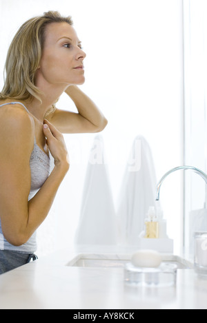 Donna in piedi dal lavandino del bagno, esame di sé nel mirror Foto Stock