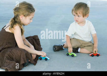 Fratello e Sorella di seduta sul terreno, giocando con Toy Cars, ragazzo accigliata a ragazza Foto Stock