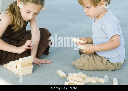 Fratello e Sorella di seduta sul terreno, giocando con la costruzione di blocchi insieme Foto Stock