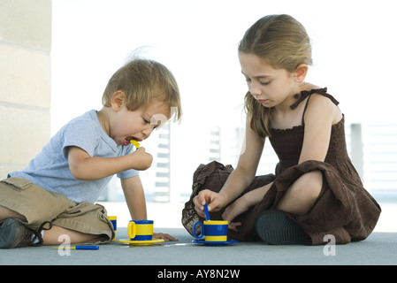 Fratello e Sorella di seduta sul terreno, giocando con plastica teacups insieme Foto Stock