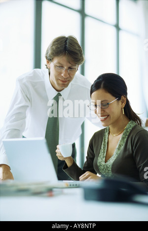 Maschio e femmina cerca colleghi al computer portatile insieme, donna azienda tazza da caffè Foto Stock