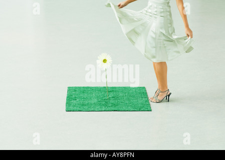 Donna abito in piedi accanto a gerbera daisy crescono fuori del tappeto erboso artificiale, vista ritagliata Foto Stock