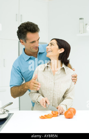 Matura in cucina, sorridente ad ogni altra donna per affettare il pomodoro con il coltello Foto Stock