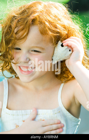 Bambina di conchiglia di contenimento fino a orecchio, sorridente, guardando lontano Foto Stock