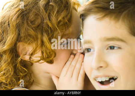 Bambina sussurra nel suo fratello l'orecchio, close-up Foto Stock