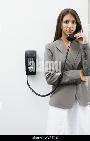 Ragazza adolescente utilizzando montato a parete telefono fisso, guardando la fotocamera Foto Stock