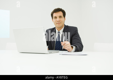 Imprenditore seduto alla scrivania, utilizzando il computer portatile, sorridente in telecamera Foto Stock