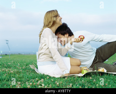 Giovane seduti insieme sulla coperta picnic, ridendo, donna azienda apple Foto Stock