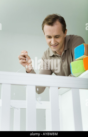 Uomo appoggiato sopra la culla, azienda mobile, guardando verso il basso Foto Stock