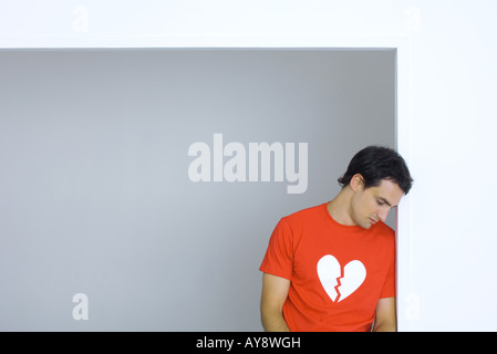 Uomo che indossa tee-shirt con cuore spezzato simbolo, guardando verso il basso Foto Stock