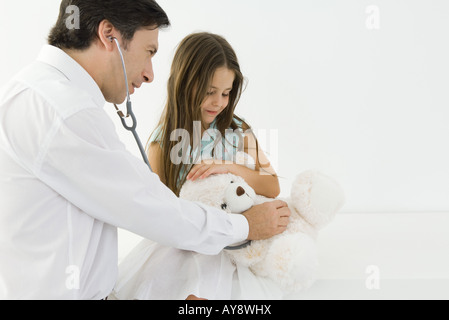 Medico seduto con bambina, esaminando orsacchiotto con uno stetoscopio Foto Stock