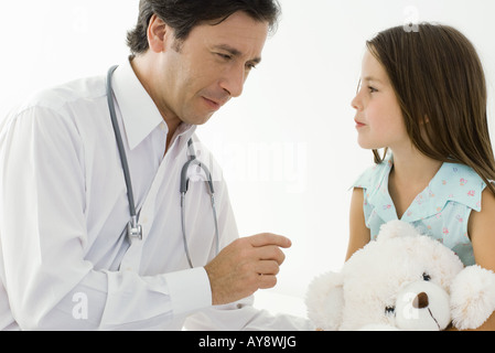 Medico seduto con bambina, ragazza con Teddy bear Foto Stock