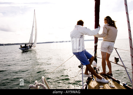 Coppia giovane sulla parte anteriore di yacht a vela a Cowes, Isle of Wight, Regno Unito Foto Stock