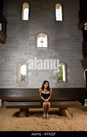 Una sposa in un abito nero seduta su una panchina all'interno di un castello medievale Foto Stock