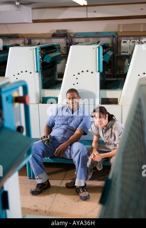 Ritratto di un uomo e di una donna in tute seduti nella parte anteriore di una macchina da stampa Foto Stock