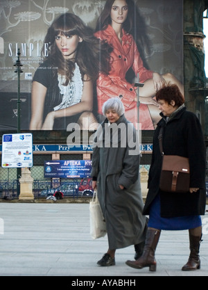 Un paio di donne anziane a piedi attraverso una piazza di Cracovia con un poster grande mostra modelli giovani pubblicità moda. Foto Stock