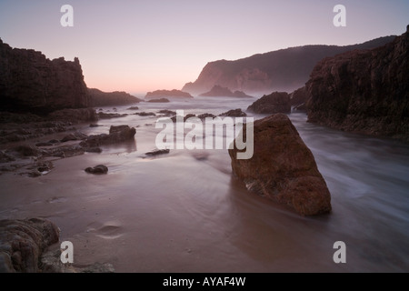 Tramonto con il mare, rocce e boluders guardando verso le teste di Knysna, Sud Africa Foto Stock