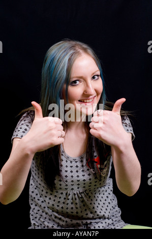 Felice white ragazza sorridente con il pollice in su contro uno sfondo nero Foto Stock