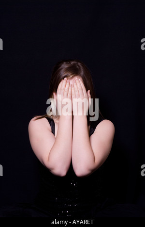 La donna nasconde il viso con le mani su di uno sfondo nero Foto Stock