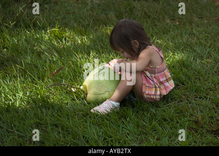 Bambina sorseggiando verde latte di cocco attraverso una cannuccia mentre è seduto sull'erba Foto Stock