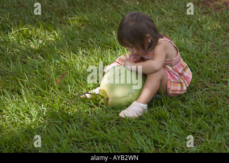 Bambina sorseggiando verde latte di cocco attraverso una cannuccia mentre è seduto sull'erba Foto Stock