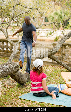 Giovane uomo allegramente camminando sul ramo di albero con la fidanzata a guardare Foto Stock