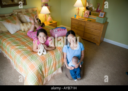 Ragazza adolescente sdraiato sul letto in camera con mamma e bambino fratello Foto Stock