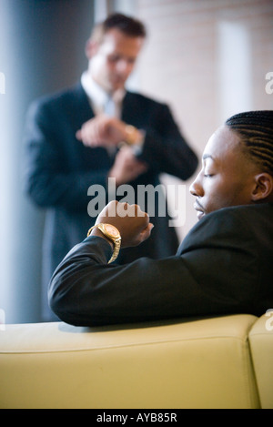La gente di affari seduti e in attesa in un ufficio lobby, guardando i loro orologi Foto Stock